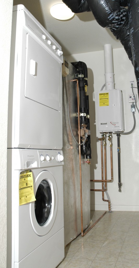 Figure 2. A whole-house tankless gas water heater installed in a laundry room with proper venting to the outdoors and a wired temperature and function controller on the wall to the right of the tankless unit. [Click image for full size version.] Credit: <a href="http://images.nrel.gov/viewphoto.php?imageId=6310913" target="_blank">Amy Glickson - Pixl Studio, Courtesy NREL</a>.